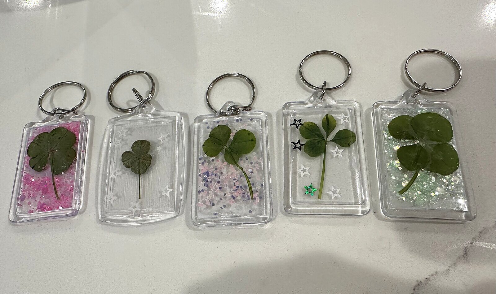 Five clover keychains lined up, each with a real pressed four-leaf clover and glitter