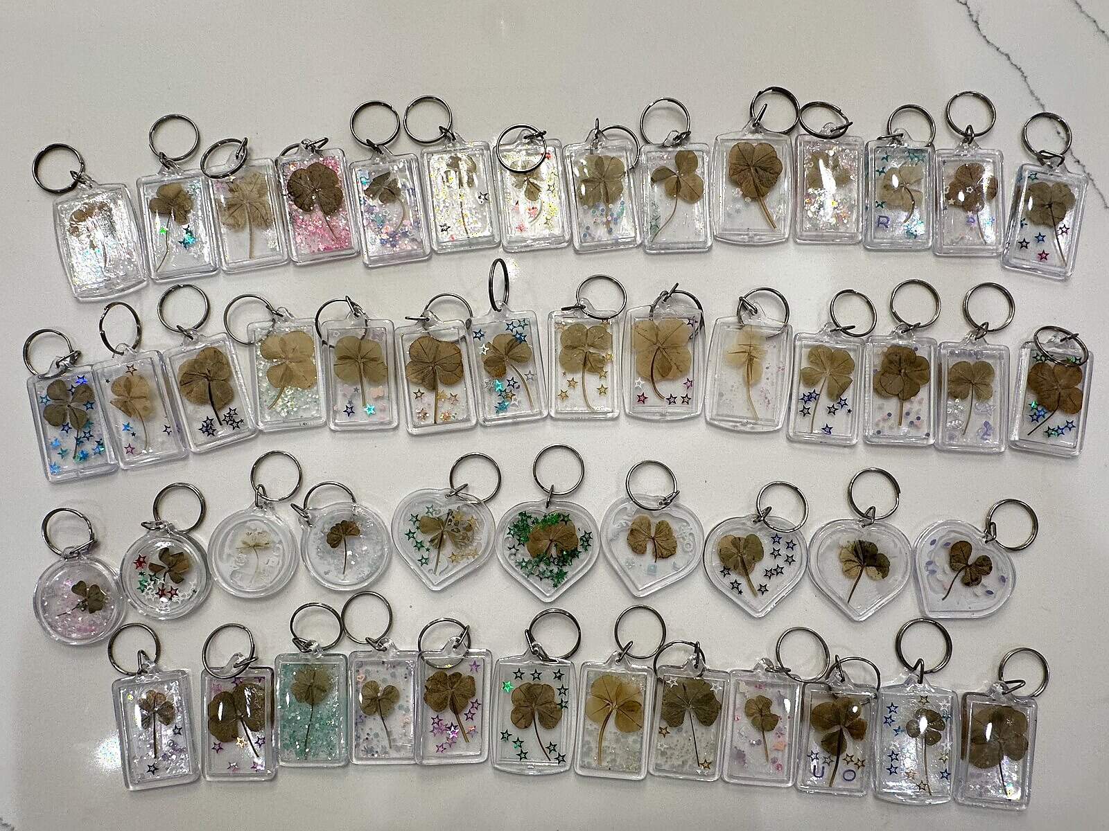Dozens of clear acrylic keychains, each holding a real pressed four-leaf clover with glitter and stars
