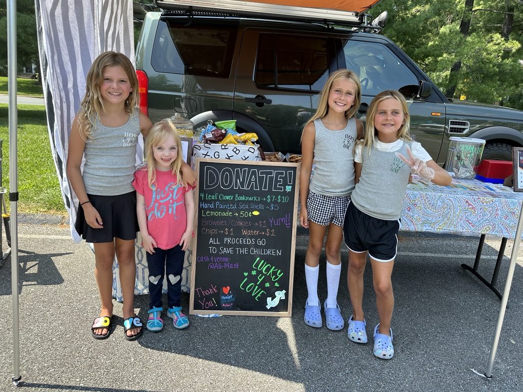Lemonade, cookies and snow cones set out on a green gingham table at a neighborhood stand
