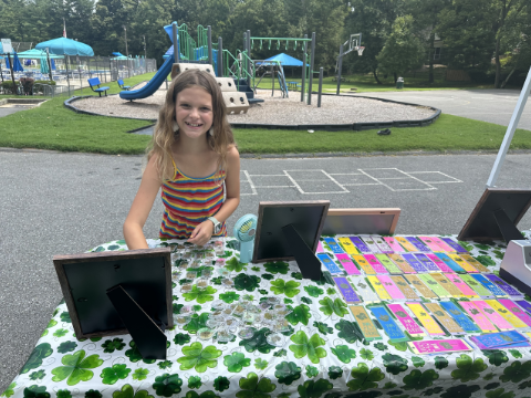 Henley, age 10, behind her clover-covered fundraising table at a 2024 Lucky4Love stand